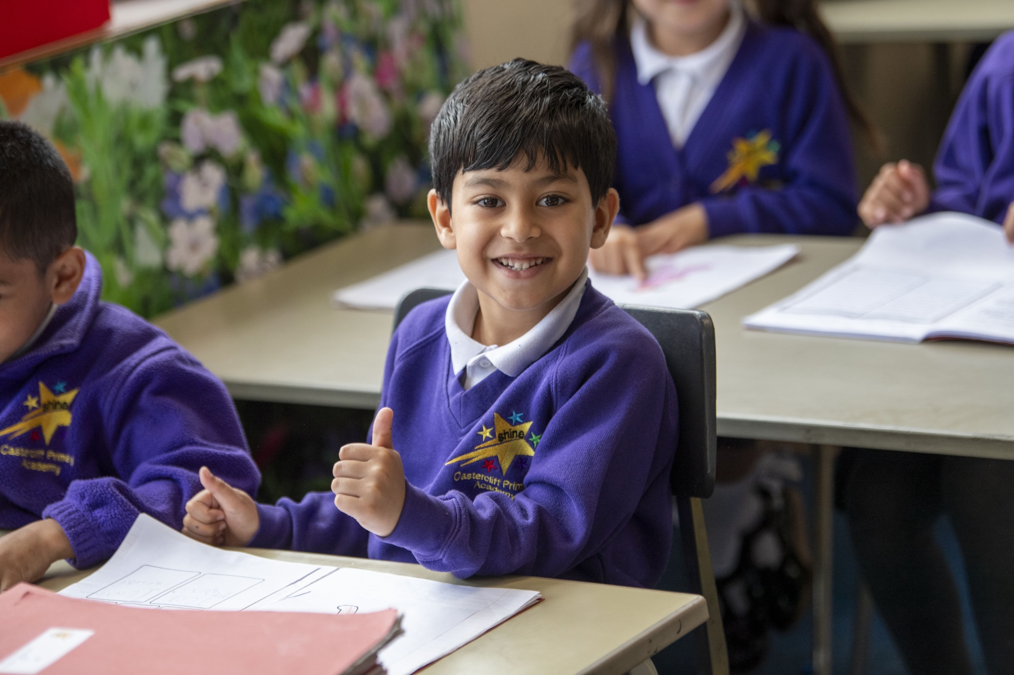 A boy in Castercliff uniform sat at a classroom desk with his thumbs up